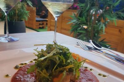 Assiette de viande garnie de roquette et sauce rouge, servie sur une table avec des verres de vin en arrière-plan.