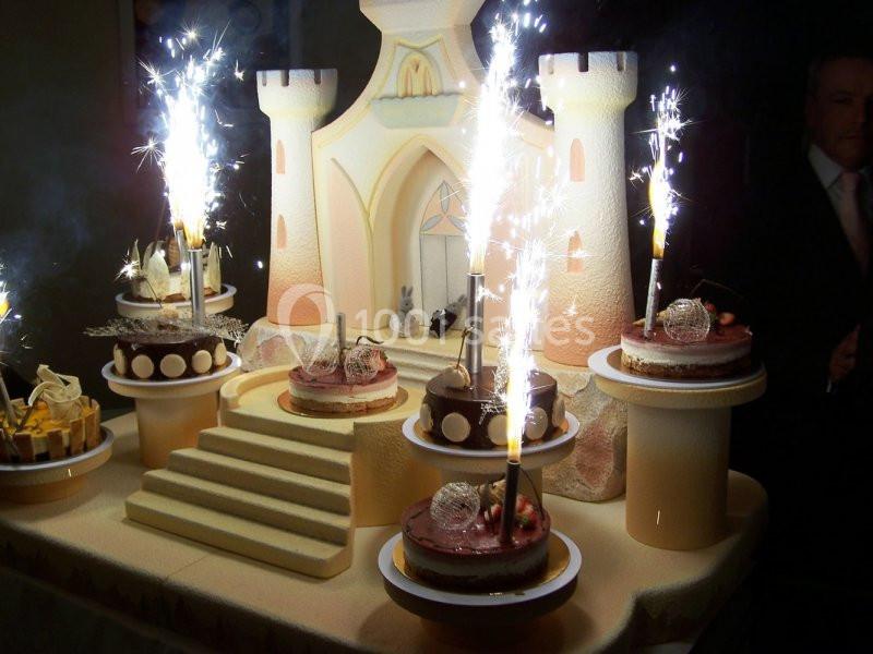 Gâteau en forme de château avec des étincelles et des desserts individuels disposés sur des supports autour.