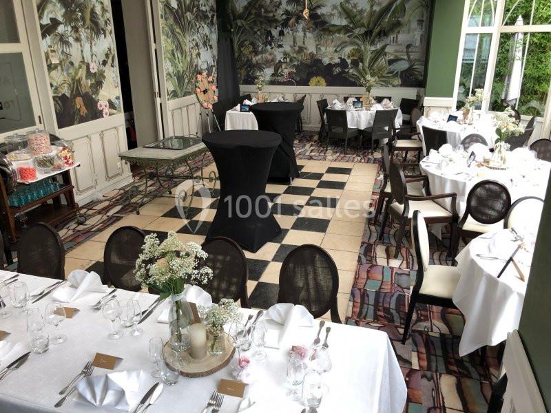 Salle de réception élégante avec tables dressées, nappes blanches et décorations florales, sol en damier.