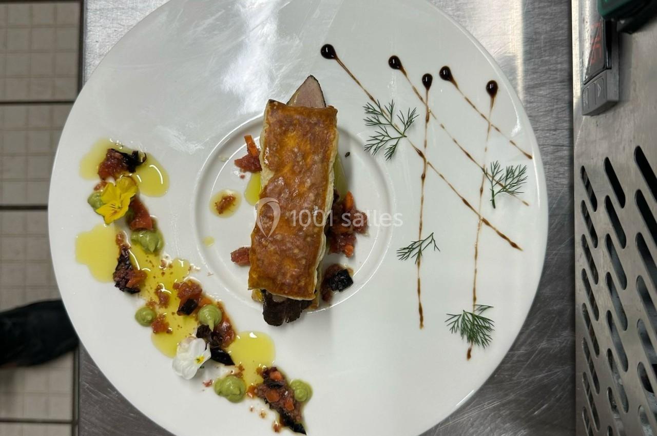 Assiette gastronomique avec viande, légumes, sauce décorative et herbes fraîches, présentée sur une table en inox.