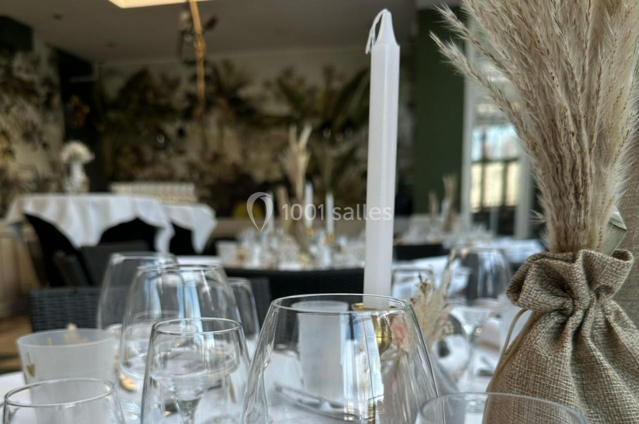 Table dressée avec des verres, bougies blanches et décoration en herbes sèches dans une salle lumineuse et élégante.