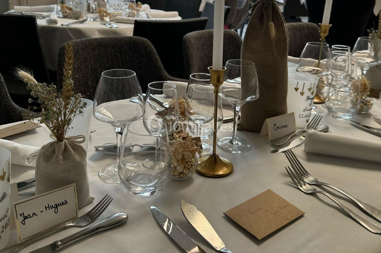 Table élégamment dressée avec vaisselle, bougies dorées, fleurs séchées et marque-places personnalisés.