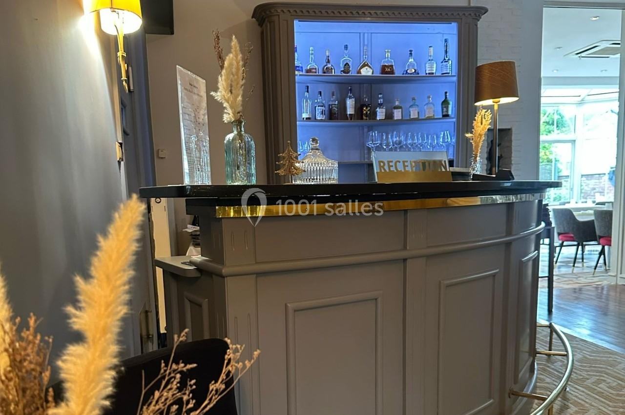 Comptoir de réception en bois avec étagères éclairées contenant des bouteilles et des verres, décoré de plantes séchées.