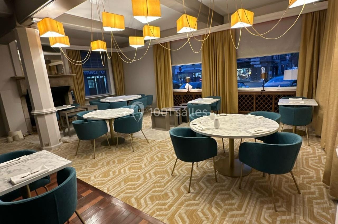 Salle de restaurant lumineuse avec tables rondes en marbre, chaises vertes et suspensions lumineuses modernes.