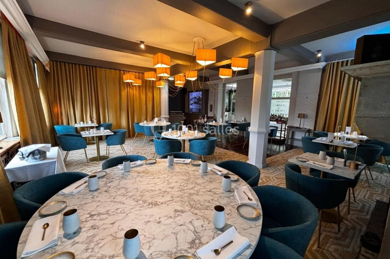 Salle de restaurant élégante avec tables rondes en marbre, chaises bleues et luminaires suspendus modernes.