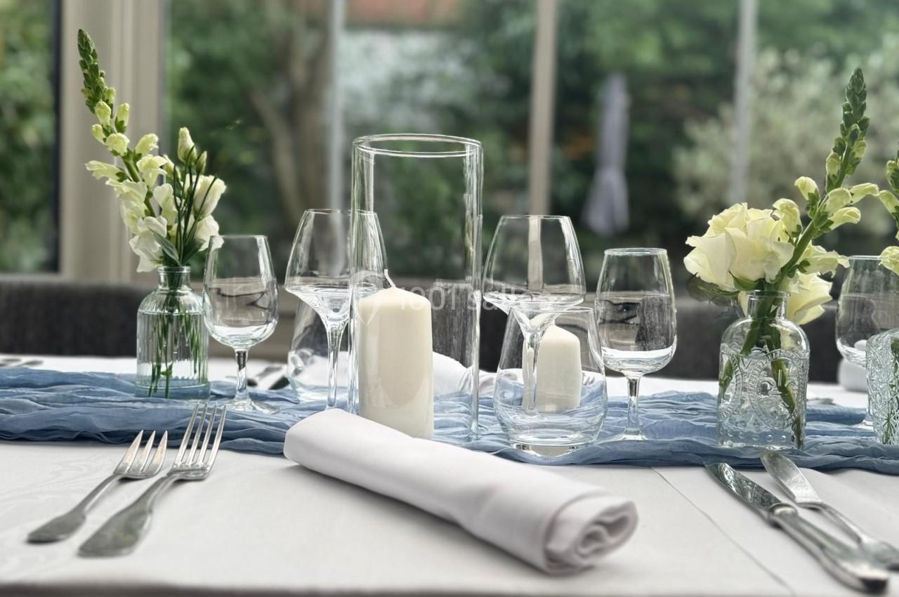 Table élégamment dressée avec verres, couverts, bougie blanche et petits bouquets de fleurs dans un cadre lumineux.