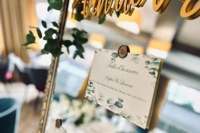 Comptoir de réception en bois avec étagères éclairées contenant des bouteilles et des verres, décoré de plantes séchées.