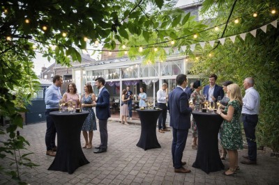 Comptoir de réception en bois avec étagères éclairées contenant des bouteilles et des verres, décoré de plantes séchées.