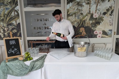 Comptoir de réception en bois avec étagères éclairées contenant des bouteilles et des verres, décoré de plantes séchées.