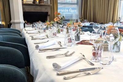 Comptoir de réception en bois avec étagères éclairées contenant des bouteilles et des verres, décoré de plantes séchées.