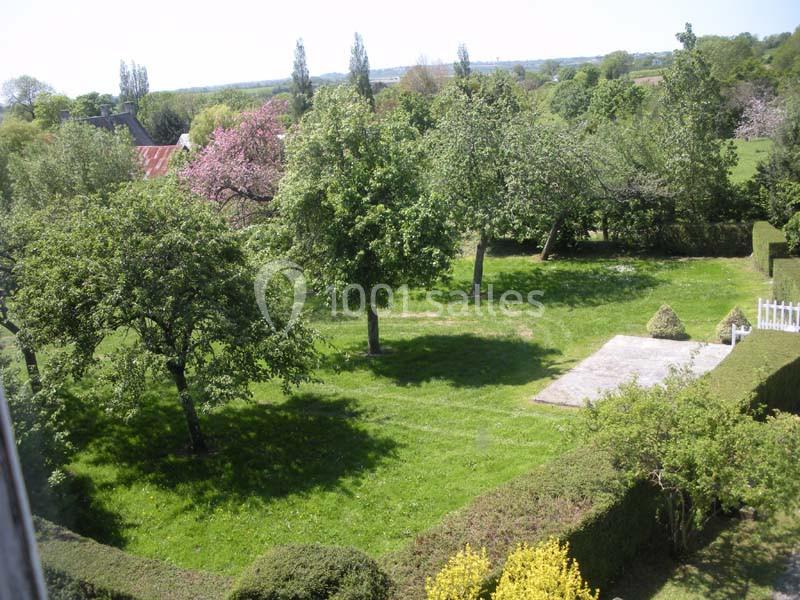 Vue d'un jardin verdoyant avec des arbres, une pelouse bien entretenue et une petite terrasse ensoleillée.