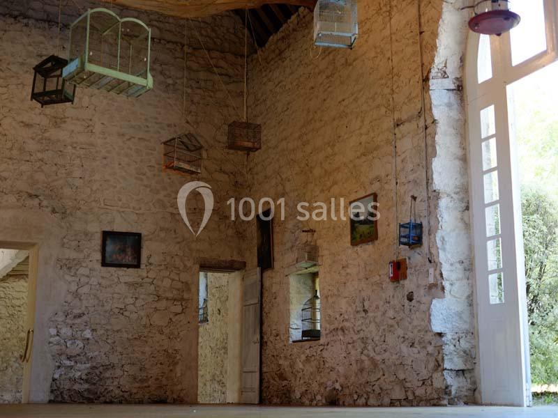 Intérieur d'une pièce en pierre avec des cages suspendues, des tableaux accrochés et une grande porte vitrée.