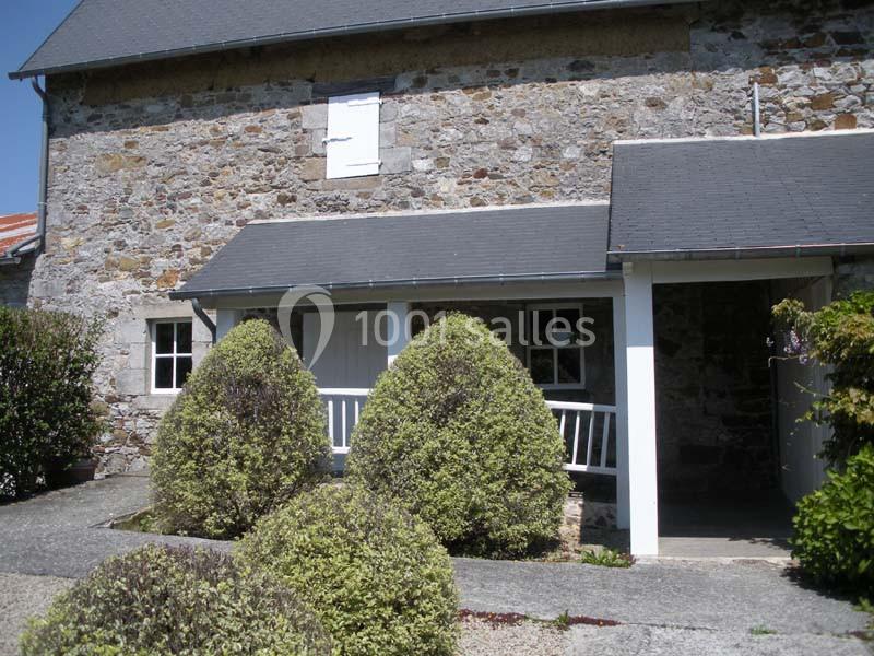 Façade en pierre d'une maison avec porche couvert, arbustes taillés et allée en gravier au premier plan.