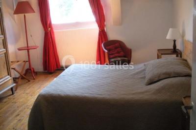 Chambre simple avec un lit double, deux lampes de chevet, des tableaux au mur et une grande fenêtre avec rideaux.