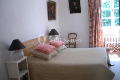 Chambre simple avec un lit double, deux lampes de chevet, des tableaux au mur et une grande fenêtre avec rideaux.