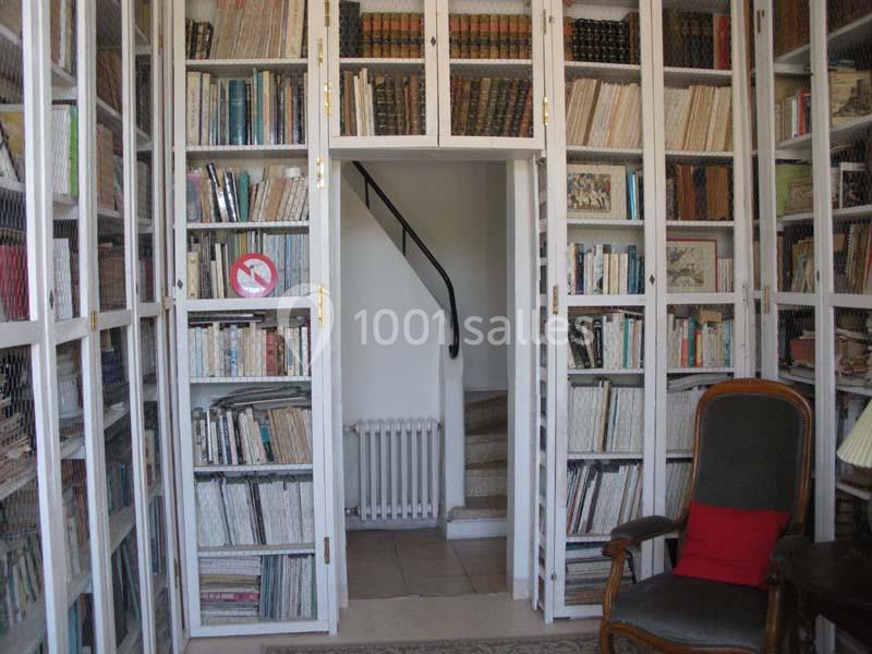 Bibliothèque avec étagères remplies de livres, une chaise avec coussin rouge et une porte menant à un escalier.