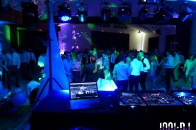 Vue d'une soirée dansante avec une piste éclairée, des invités et une table de mixage au premier plan.