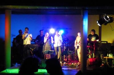 Un groupe de musiciens et chanteurs se produit sur une scène éclairée par des lumières colorées.