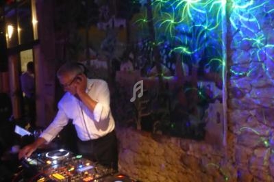 Un DJ mixe sur une table de mixage dans une ambiance lumineuse avec des projections colorées sur un mur en pierre.