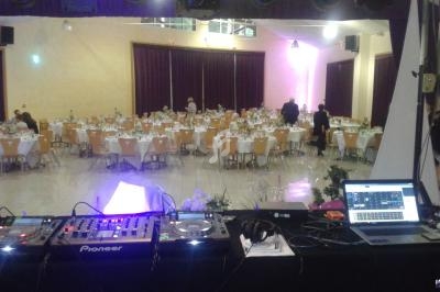 Salle de réception décorée avec des tables dressées, vue depuis une table de mixage avec équipements DJ au premier plan.