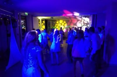 Des personnes dansent dans une salle éclairée par des lumières colorées, créant une ambiance festive.