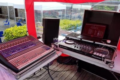Table de mixage et platines DJ installées en extérieur sous une tente rouge, avec des équipements audio visibles.