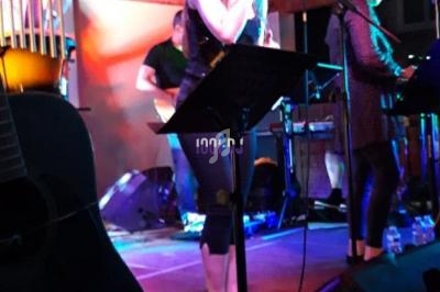 Une chanteuse se produit sur scène avec des musiciens, éclairée par des lumières colorées dans une ambiance chaleureuse.