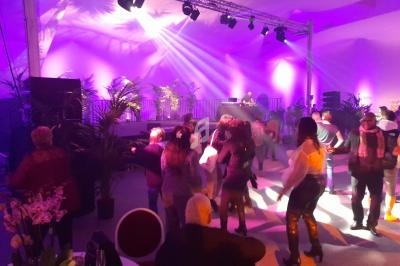 Personnes dansant sous des lumières colorées dans une salle avec un DJ sur une scène en arrière-plan.