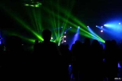 Silhouettes de personnes dans une salle sombre éclairée par des faisceaux lumineux verts et bleus.