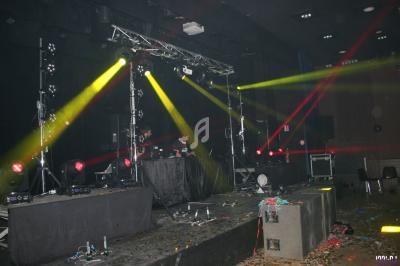 Scène de concert vide avec jeux de lumières colorées, équipements techniques et sol jonché de débris.