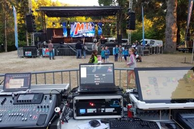 Poste de régie technique avec consoles et ordinateurs, face à une scène extérieure en préparation pour un événement.