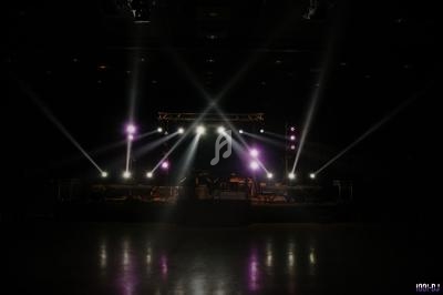 Scène de concert vide éclairée par des projecteurs lumineux dans une salle sombre.