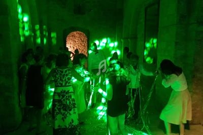 Des personnes dansent dans une salle en pierre éclairée par des lumières vertes diffusant un effet festif.