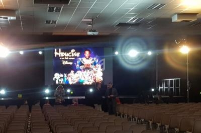 Salle de conférence avec des rangées de chaises vides et un écran affichant une affiche lumineuse de film.