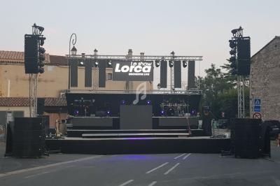 Scène extérieure équipée de projecteurs, écrans et instruments, installée sur une place entourée de bâtiments en pierre.