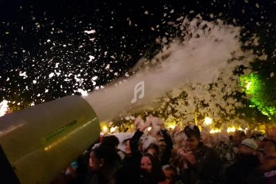 Un canon à mousse projette de la mousse sur une foule en fête, éclairée par des lumières nocturnes.