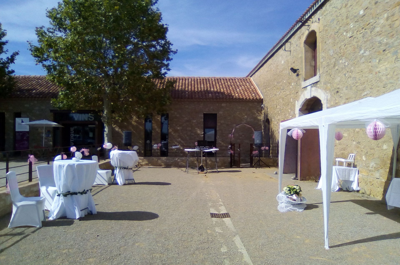Cour extérieure aménagée pour un événement avec tables décorées, tonnelle blanche et bâtiment en pierre en arrière-plan.