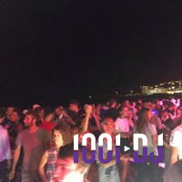 Foule dansante en extérieur de nuit, éclairée par des lumières colorées, avec des bâtiments illuminés en arrière-plan.