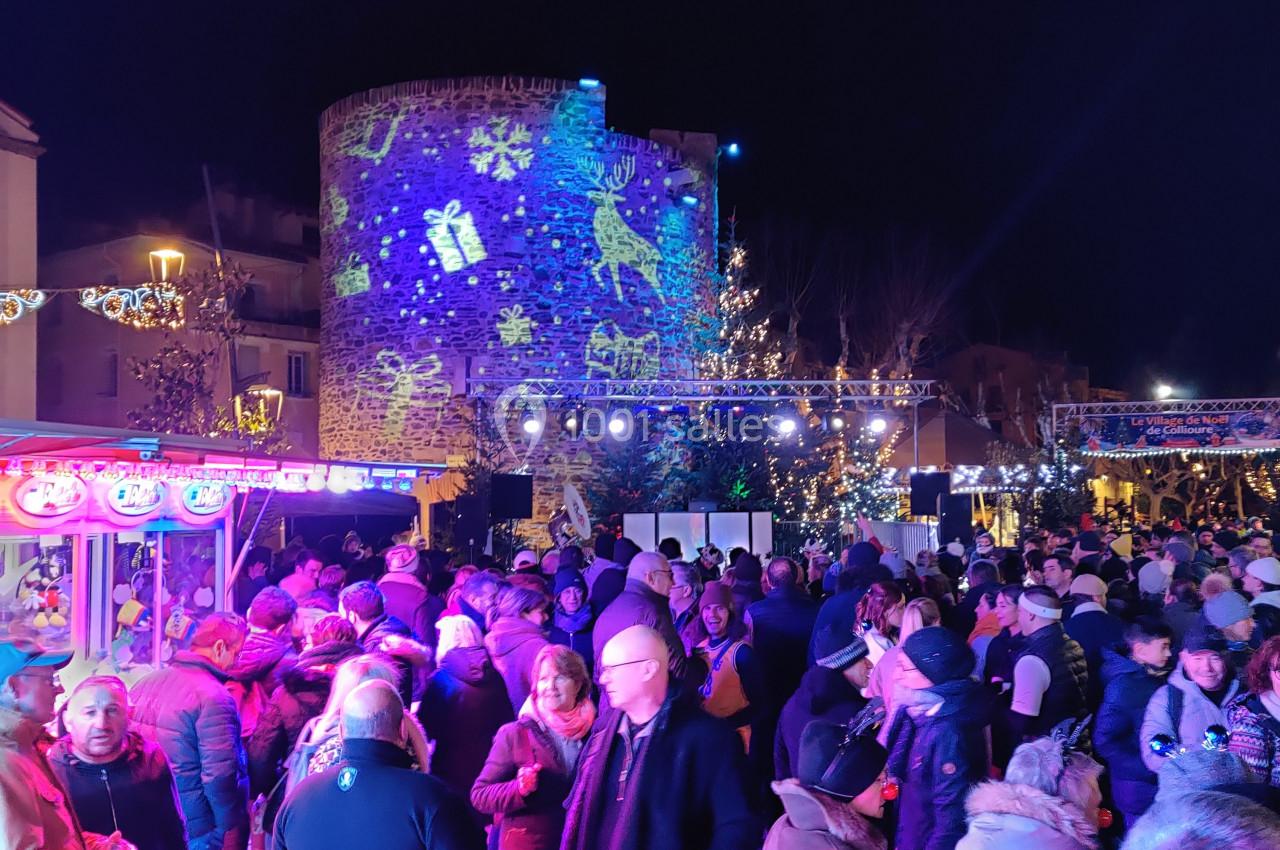 Foule rassemblée de nuit devant une tour illuminée de projections festives, entourée de décorations de Noël.