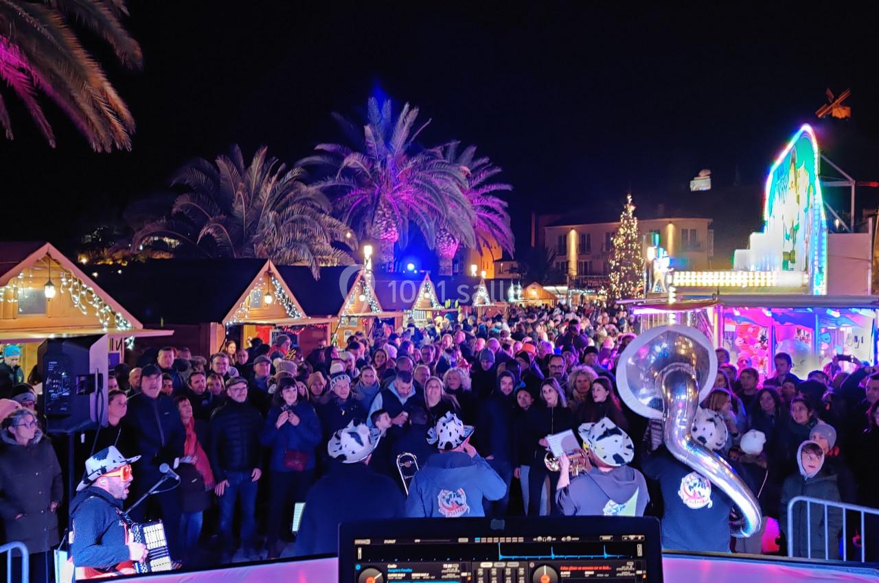 Foule rassemblée devant des stands illuminés lors d'un événement nocturne, avec un DJ en premier plan.