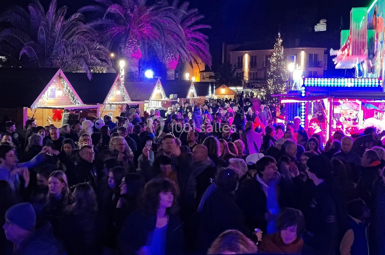 Foule rassemblée de nuit dans un marché de Noël illuminé, avec chalets décorés et ambiance festive.