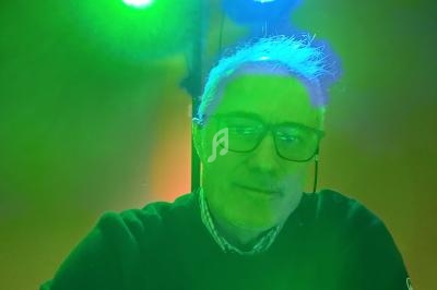 Homme portant des lunettes, éclairé par des lumières vertes et bleues dans un environnement intérieur.