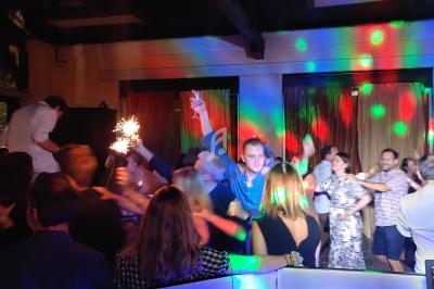 Groupe de personnes dansant sous des lumières colorées dans une salle sombre avec des rideaux dorés en arrière-plan.
