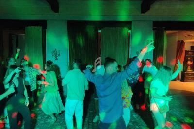 Des personnes dansent sous des lumières colorées dans une salle sombre, avec une table de mixage au premier plan.