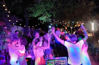 Personnes dansant et socialisant en extérieur la nuit, éclairées par des guirlandes lumineuses et des lumières colorées.