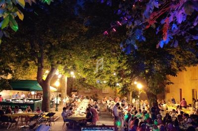 Vue depuis une scène avec un ordinateur de mixage, éclairages colorés et des convives dînant en plein air sous des arbres.