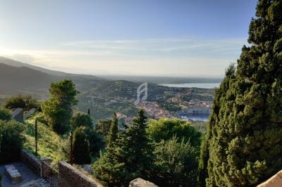 Vue panoramique sur une ville côtière entourée de collines verdoyantes et d'arbres, avec la mer à l'horizon.