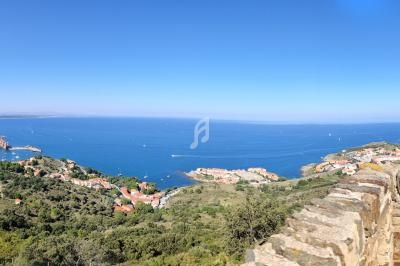 Vue panoramique sur une côte méditerranéenne avec villages, collines verdoyantes et mer bleue sous un ciel dégagé.