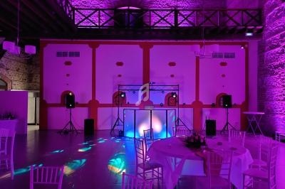 Salle de réception éclairée par des lumières violettes, avec des tables dressées et une piste de danse équipée.