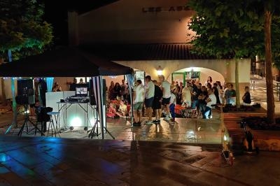 Groupe de personnes rassemblées en soirée sur une place éclairée, près d'un stand avec équipement audio.